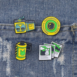 Retro camera and film roll enamel pins set displayed on classic blue denim jacket pocket