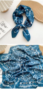 Close-up of a navy blue silk scarf featuring white paisley and floral prints in a flat lay