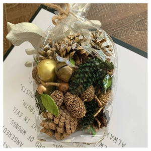 Close-up of festive DIY pine cone set with gold bells and ornaments in clear gift bag