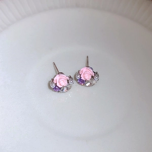 Dettaglio di orecchini a rosa rosa con perle e cristalli su un piatto bianco liscio
