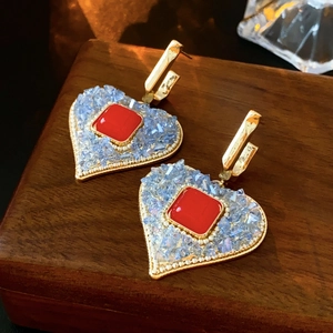 Detail of red square crystal heart earrings with blue accents on dark wood