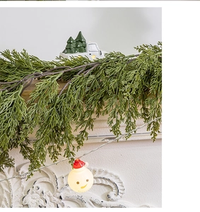 Close-up of artificial cypress garland with glowing snowman light and ceramic truck decor