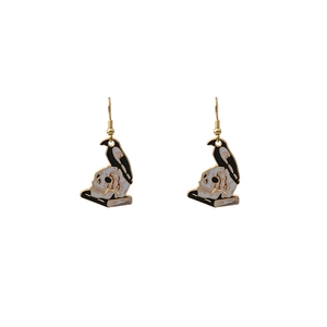 Detail of gothic raven perched on a skull and books hanging hook earrings jewelry
