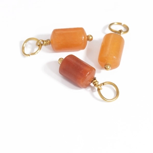 Three cylindrical orange and reddish natural stone pendants with gold metal rings