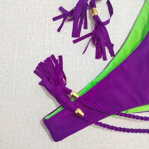 Detail of purple bikini bottom featuring neon green lining and tassel charm with metal ends