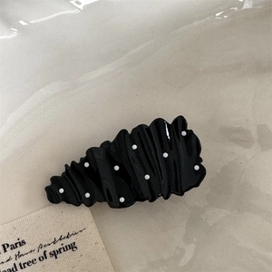 Close-up of wavy black hair clip with white polka dots and high-gloss finish texture