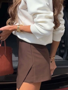 Detail of white crewneck knit sweater with embroidery and brown asymmetrical skirt