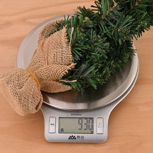 Primo piano di un mini albero di Natale da 30cm che pesa 930g su una bilancia da cucina