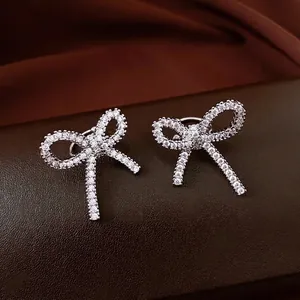 Elegant bow-shaped silver stud earrings paved with sparkling zircon on leather surface