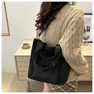 Side view of a large black nylon tote bag with dual handles and adjustable shoulder strap
