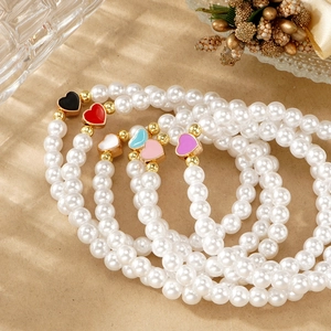 Detalle de pulseras de perlas blancas con colgantes de corazones de colores y oro