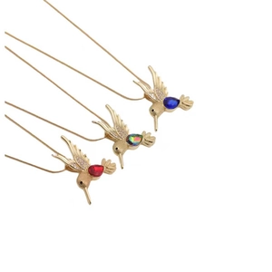Trois colliers colibri dorés avec des pierres bleues, arc-en-ciel et rouges sur fond blanc