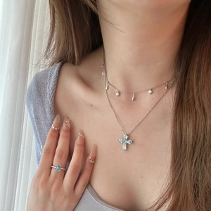 Detail of light blue cross pendant necklace and matching gemstone ring on model