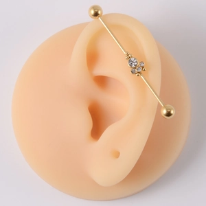 Close-up of golden industrial barbell earring with clear gemstones on a silicone ear model
