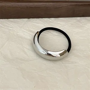 Close-up of minimalist hair tie with silver curved metal piece on beige paper