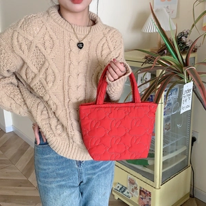 Close-up of a red quilted hand-held bag with soft heart patterns in a lifestyle setting