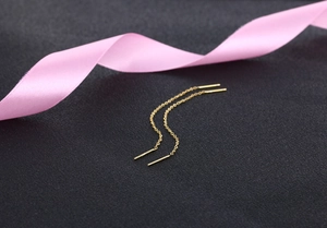 Detailed view of minimalist gold tassel chain earrings on textured background with ribbon