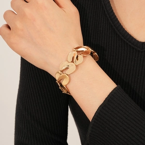 Detailed close-up of a gold S-shaped metallic elastic bracelet worn on a female wrist