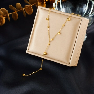 Elegant gold ball bead tassel necklace displayed on a jewelry box with silk background