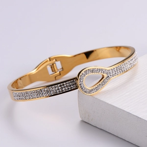 Detail of gold-plated bracelet with pavé rhinestones on a white textured background