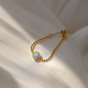 Macro detail of adjustable gold bead chain ring with round opal showing colorful fire