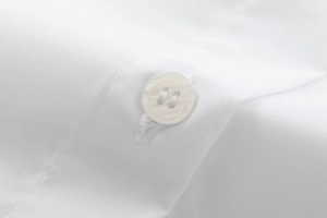 Macro shot of white four-hole resin button and clean stitching on cotton shirt fabric