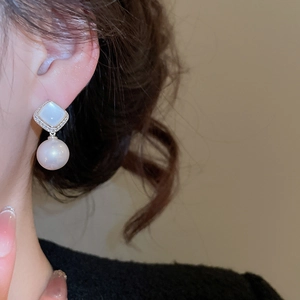 Detail of elegant pearl earrings with square stone and diamonds on a model side profile