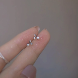 Minimalist silver wave stud earrings with three zircon stones shown on a fingertip