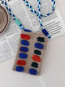 Artistic plush woven crossbody phone bag with colorful tufted decor on newspaper