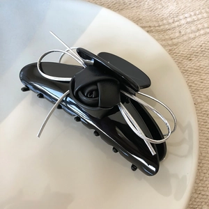 Detail of black leather rose hair clip with silver ribbon bow on a ceramic plate