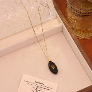 Vue détaillée d'un collier doré avec un pendentif ovale noir et une pierre rouge