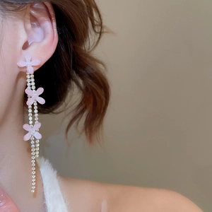 Close-up of pink resin flower earrings with long shimmering tassel chains on a model