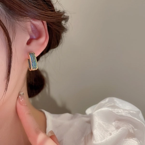 Close-up of golden rectangular huggie earrings with pavé-set teal blue zircons on model