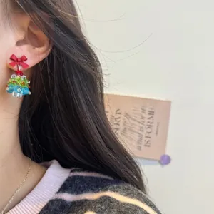 Close-up of beaded Christmas tree earrings with red bow on a model's ear
