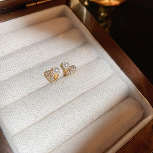 Close-up of gold heart earrings with sparkling cubic zirconia and pearls in a velvet box