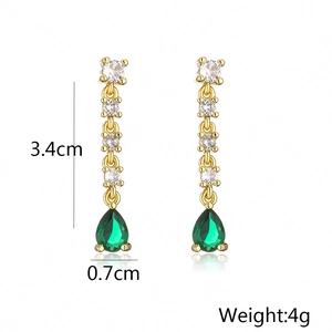 Detail view of gold tassel earrings with clear zircons and a green teardrop stone