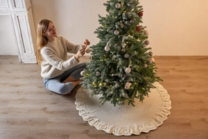 Detail of large cream knitted Christmas tree skirt with elegant wavy edges in home setting