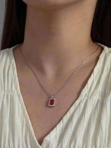 Close-up of elegant silver necklace with emerald cut red gemstone pendant on model