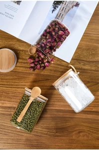 Three glass storage jars with bamboo lids and spoons on a dark wood background