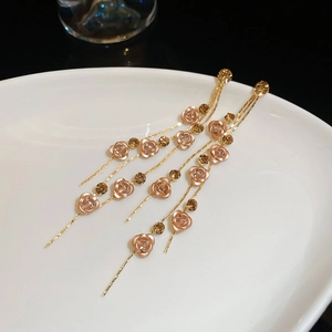 Gros plan détaillé des boucles d'oreilles à pompons dorés avec roses roses et cristaux