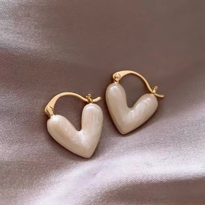 Macro shot of gold-plated heart-shaped pearl earrings on a premium silk fabric background