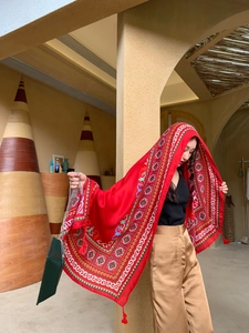 Close-up of red ethnic shawl with geometric patterns and fringe detail on clay background