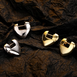 Polished gold and silver heart-shaped hoop earrings on a black textured background