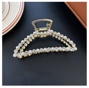 Detail of golden metal hair claw with alternating pearls and rhinestones on black background