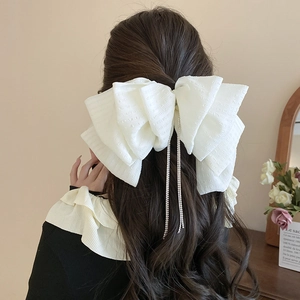 Detail shot of white lace bow hair clip featuring dangling rhinestone tassels in hair