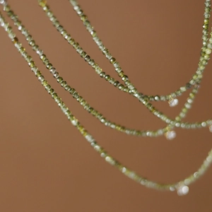 Macro detail of layered olive green zircon beads and shimmering charms on a steel chain