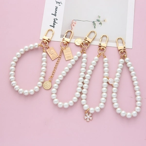 Detail of vintage faux pearl keychains with gold charms and lobster clasps on pink background
