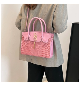 Détail de la texture crocodile rose et du pendentif lettre S dorée avec pompon du sac
