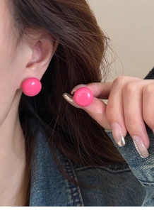 Gros plan de boucles d'oreilles rondes en résine rose vif portées avec un fond beige