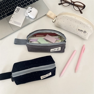 Three wool-like polka dot pencil cases in beige, grey, and blue on a modern desk